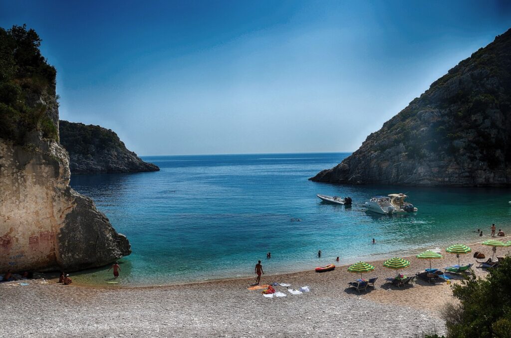 Gjiri i Gramës në Karaburun me ujë të kaltër, varka dhe shkëmbinj të lartë